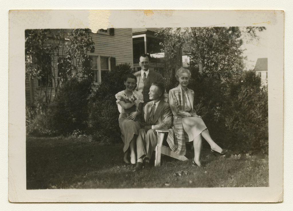 A black and white outdoor family photo of Anne Wilson, three of her family members, and a cat.