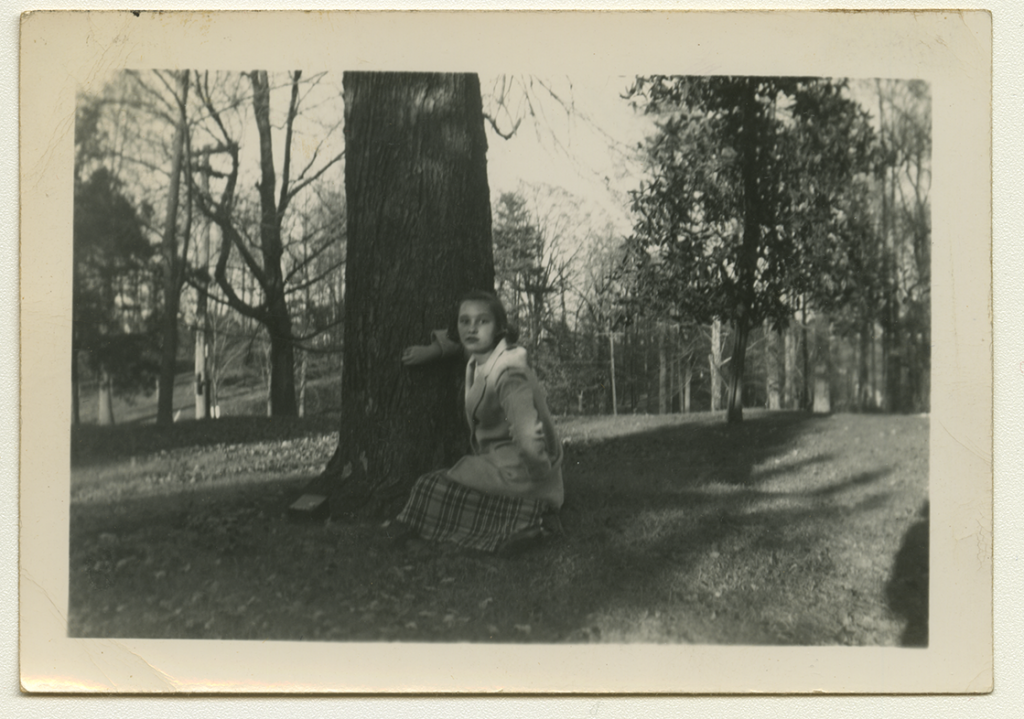 Black and white polaroid of Sandra Maynard crouched by a tree