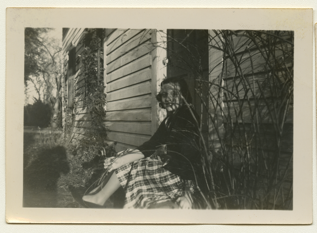 Black and white polaroid of Anne Wilson wearing a jacket and dress sitting on a porch