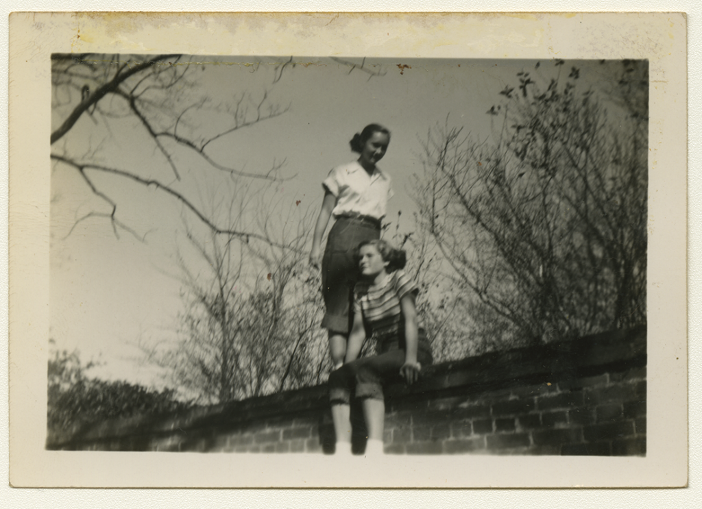 Black and white polaroid of Sandra Maynard and Alma Rowe atop a brick wall